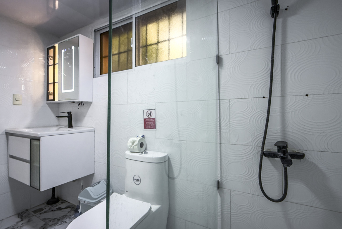 Modern white bathroom with a sleek vanity, toilet, and glass-enclosed shower.