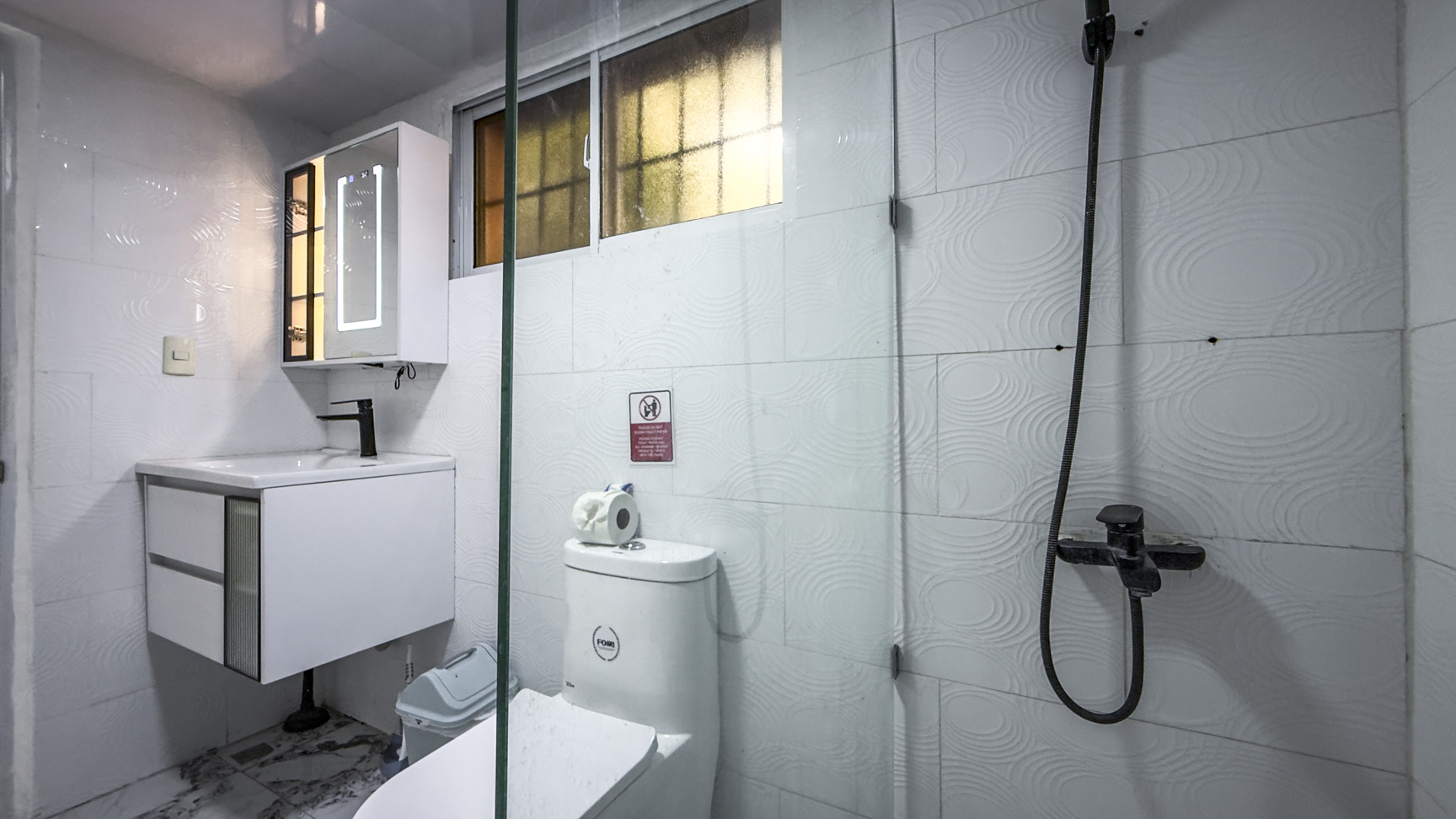 Modern white bathroom with a sleek vanity, toilet, and glass-enclosed shower.
