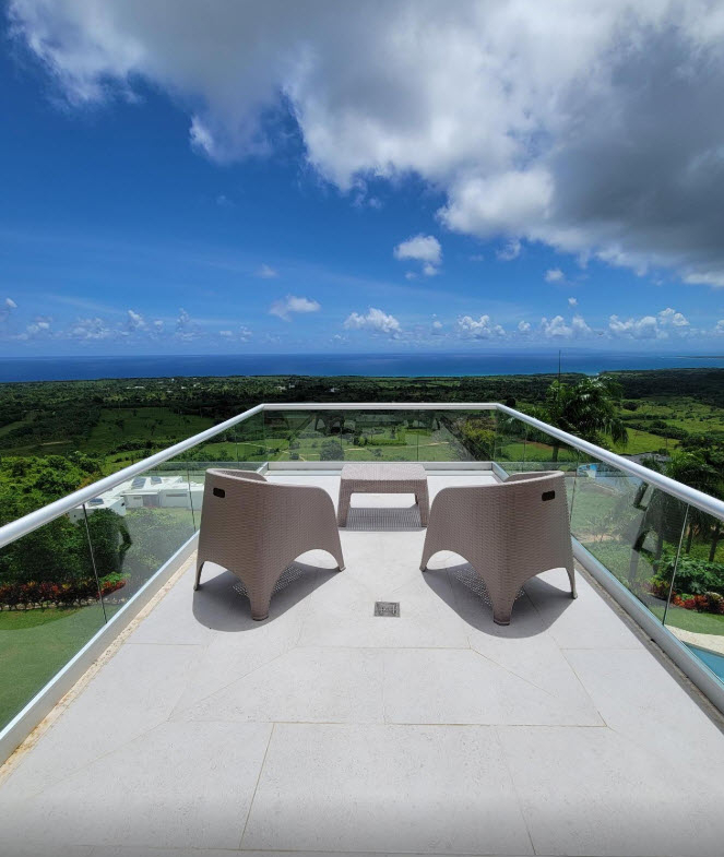 Two chairs and table on balcony overlooking lush green landscape and blue ocean