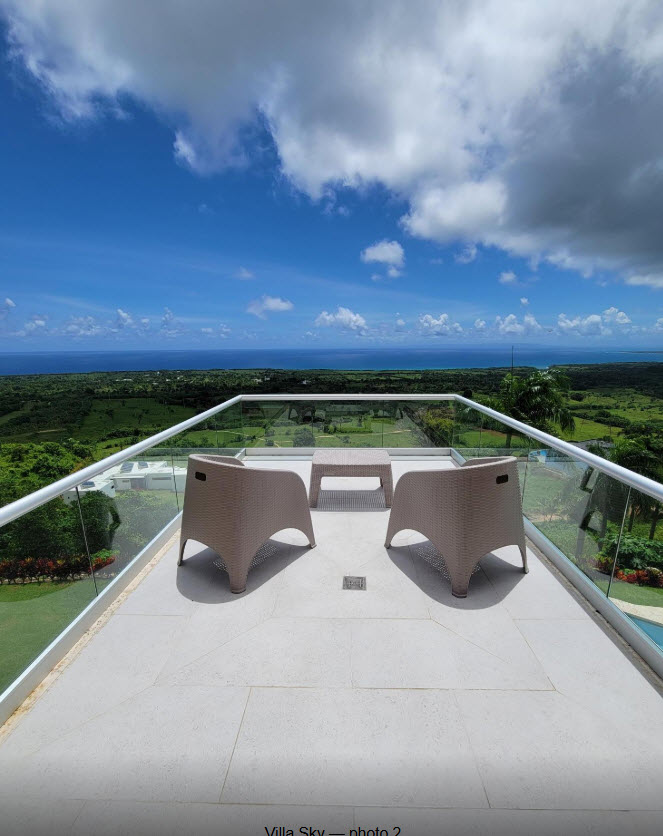 Two chairs and table on balcony overlooking lush green landscape and blue ocean