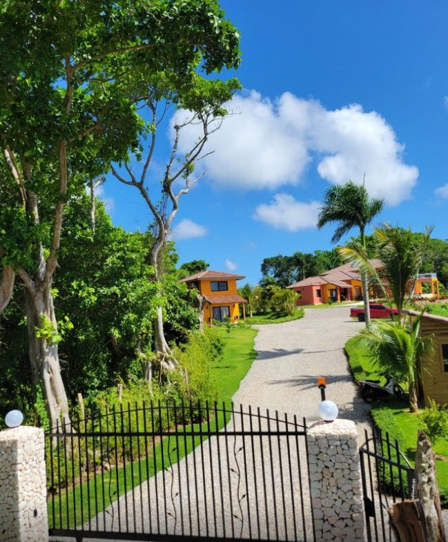 Gated entrance to vibrant orange villas surrounded by lush tropical greenery.
