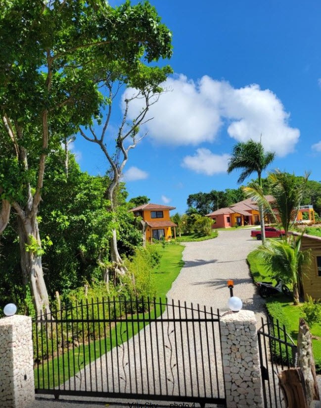 Gated entrance to vibrant orange villas surrounded by lush tropical greenery.