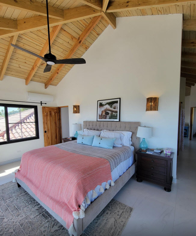 Spacious bedroom with king bed, vaulted wood ceiling, and tropical view