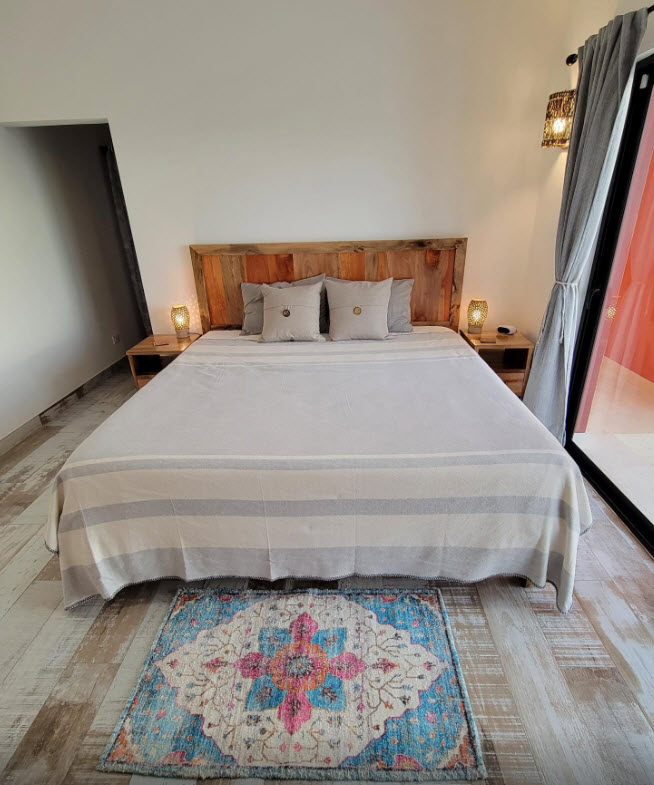 King-size bed with rustic wooden headboard, bedside lamps, and colorful rug in Villa Sky bedroom.
