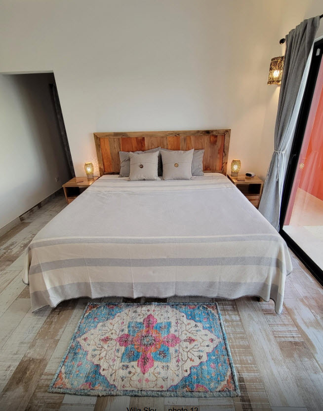 King-size bed with rustic wooden headboard, bedside lamps, and colorful rug in Villa Sky bedroom.