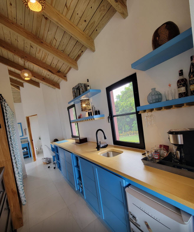 Modern kitchen with blue cabinets, wooden countertops, and a large window overlooking a garden