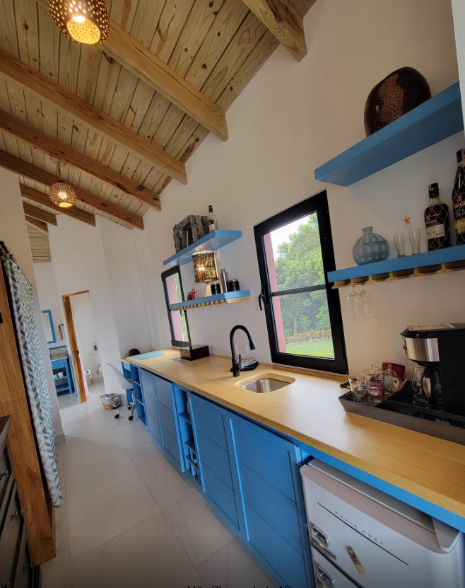 Modern kitchen with blue cabinets, wooden countertops, and a large window overlooking a garden