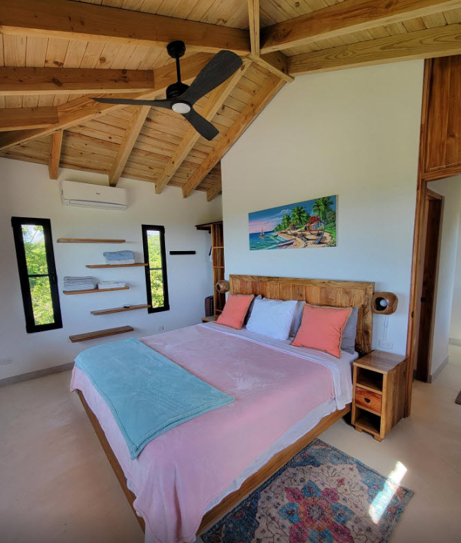 Cozy bedroom with a king-size bed, wooden accents, and a tropical painting.
