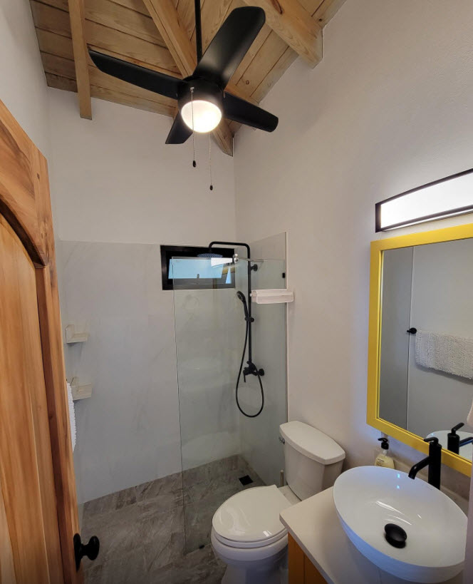 Modern bathroom with glass shower, white toilet, and yellow-framed mirror