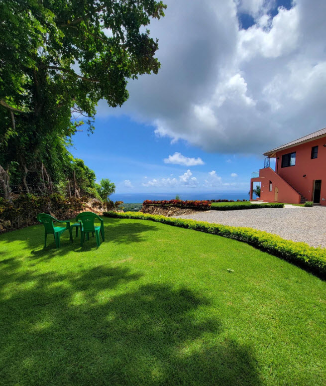 Red villa with ocean view and green chairs on manicured lawn