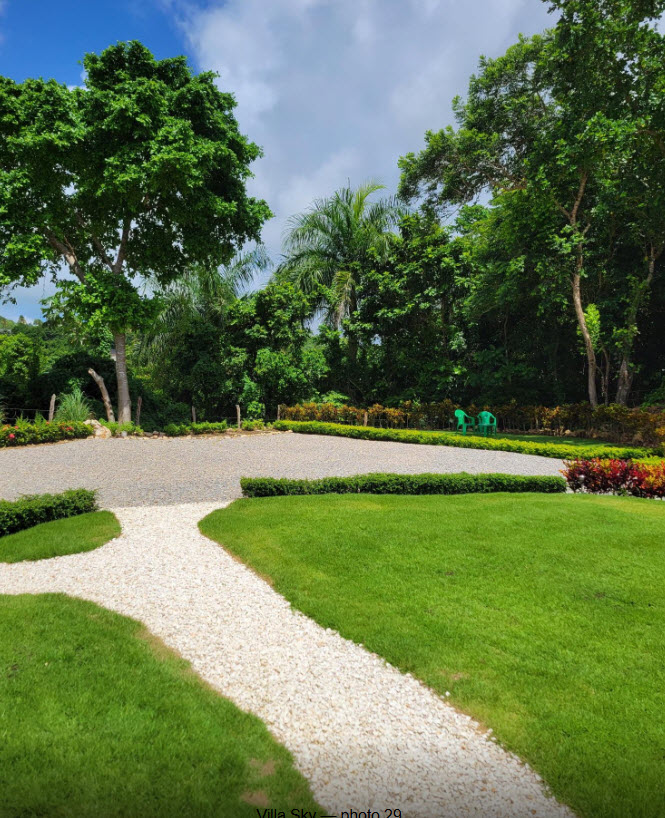 Lush green lawn and white gravel path leading to a tropical villa