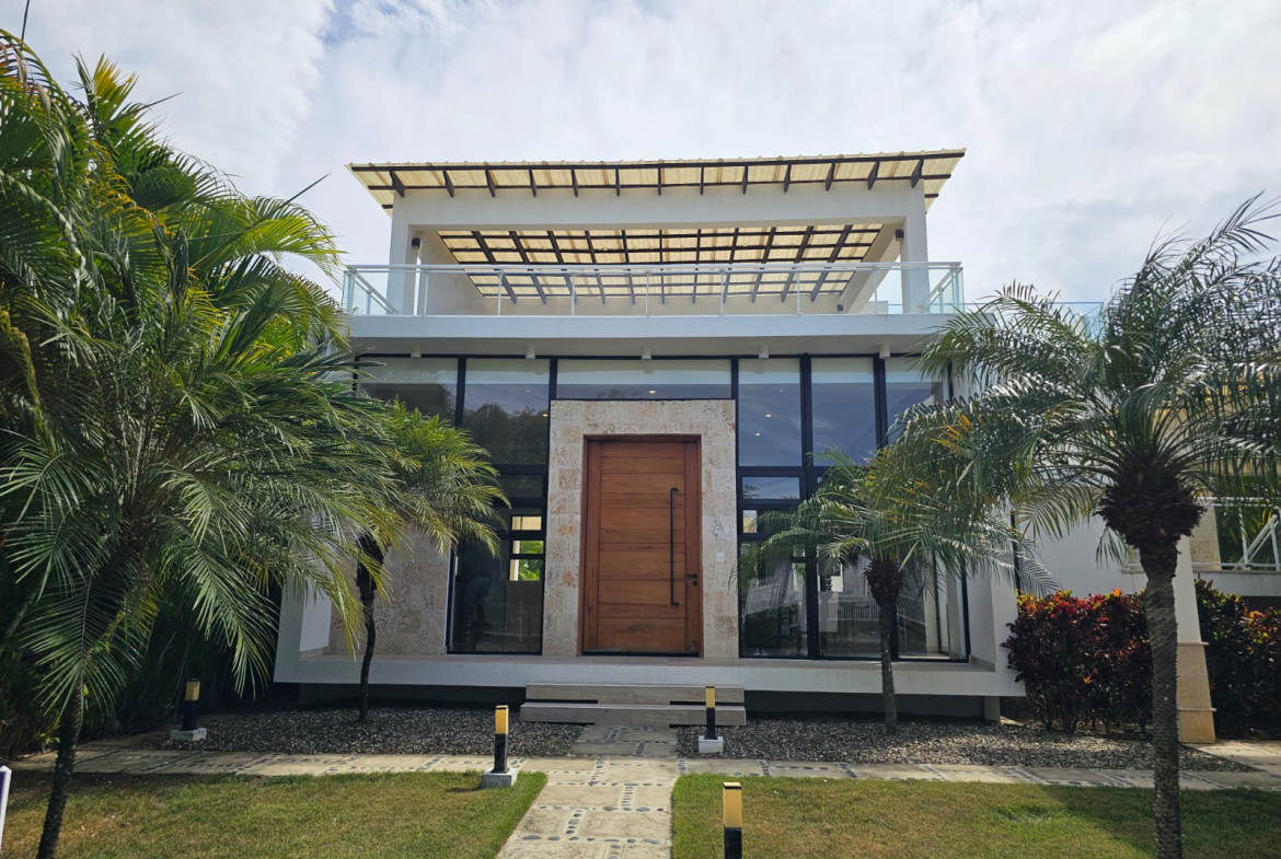 Modern white house with large glass windows and a wooden door, surrounded by palm trees.