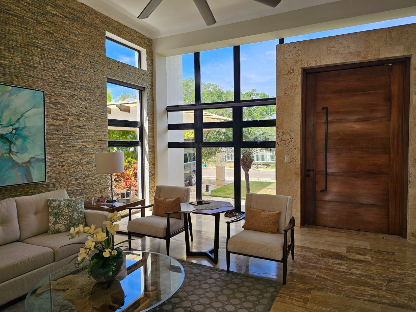 Modern living room with large windows, stone accent wall, and tropical view.