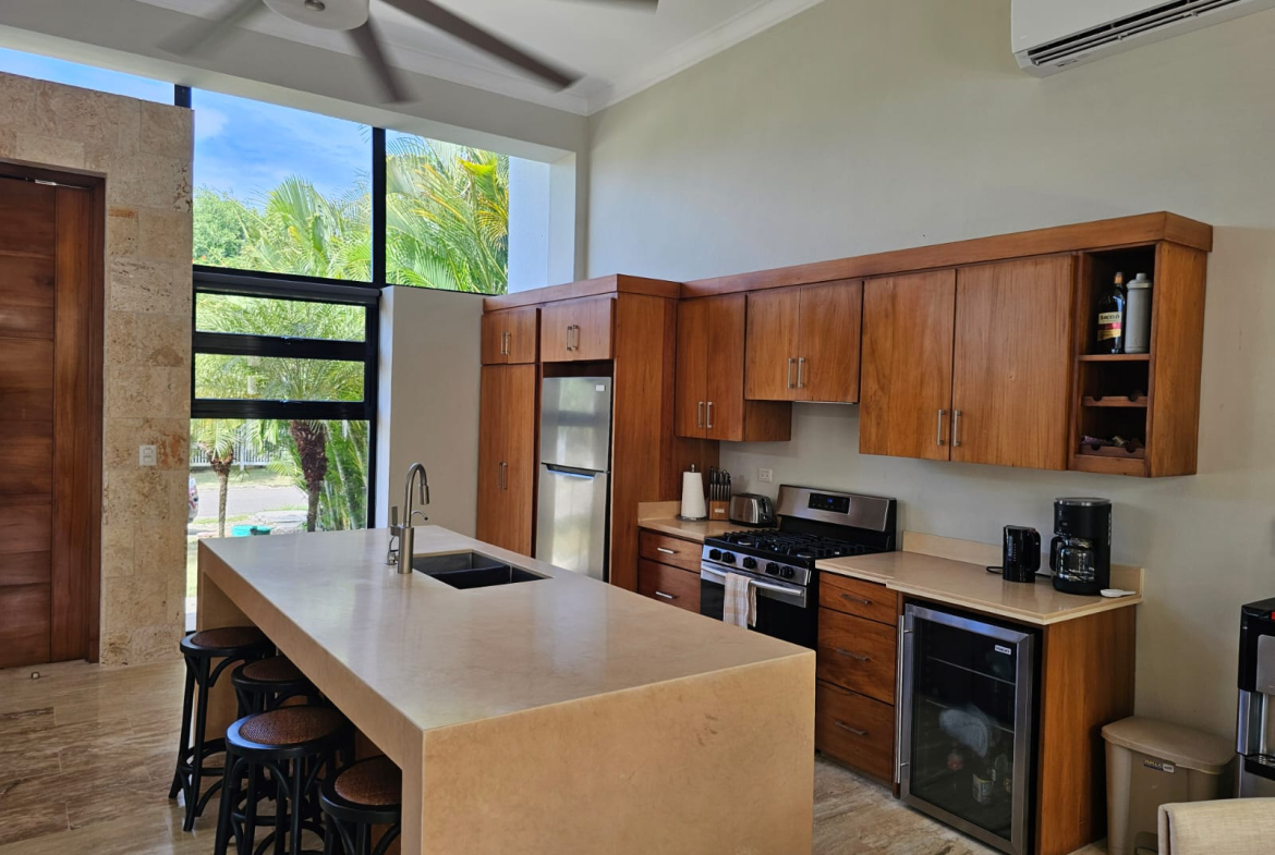 Modern tropical kitchen with large island, wood cabinets, and stainless steel appliances.