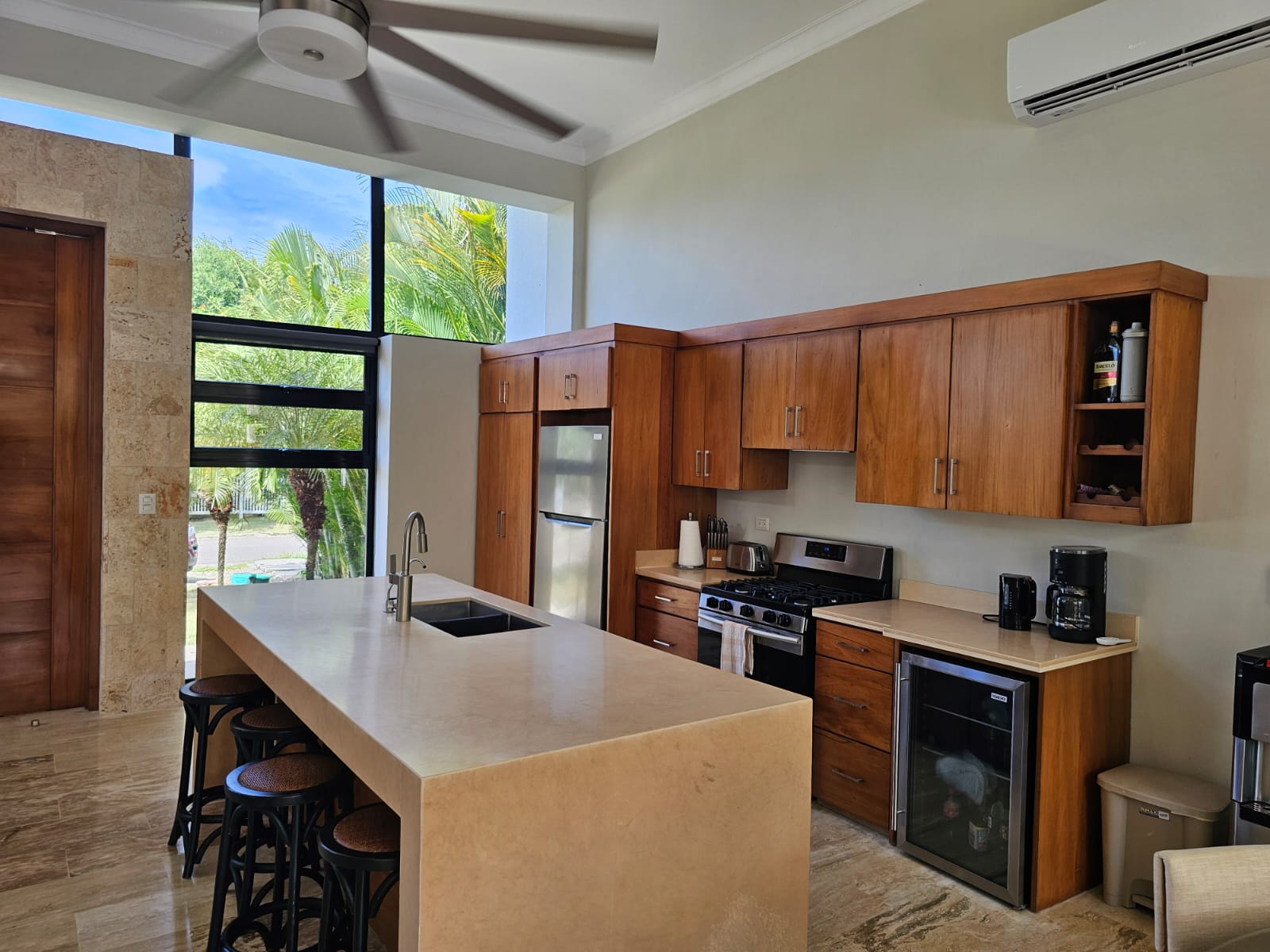 Modern tropical kitchen with large island, wood cabinets, and stainless steel appliances.