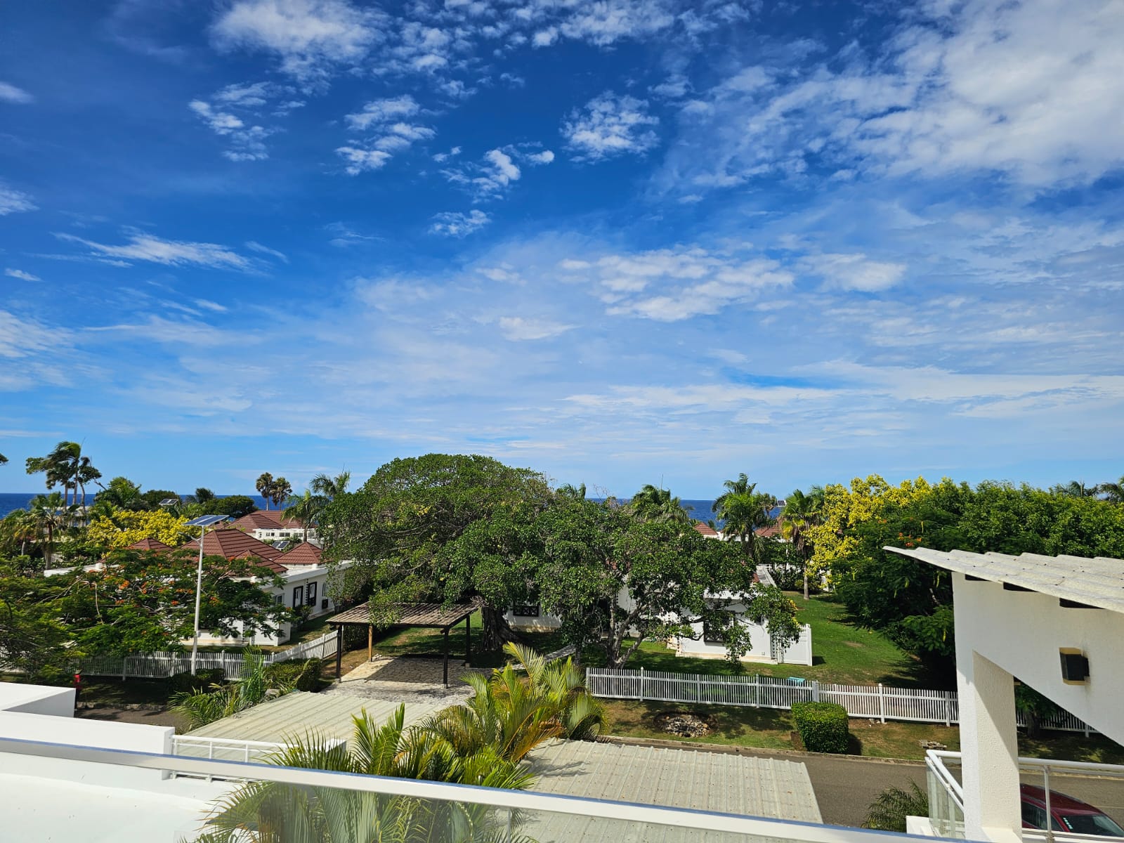 Tropical resort with white buildings, lush trees, and blue ocean under a cloudy sky.