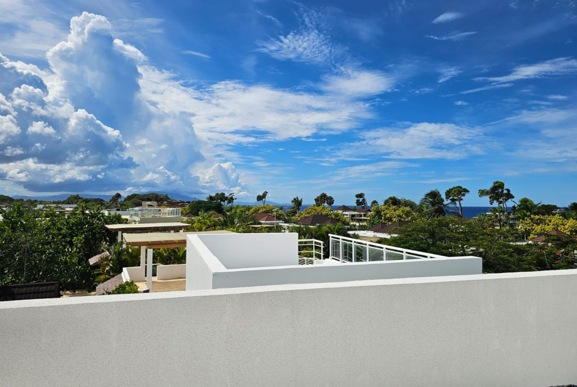 Modern white villa overlooking lush greenery and the ocean under a blue sky