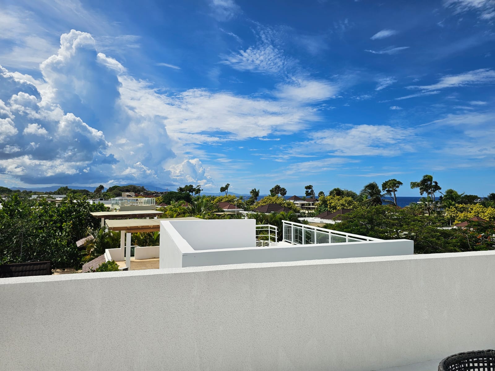 Modern white villa overlooking lush greenery and the ocean under a blue sky