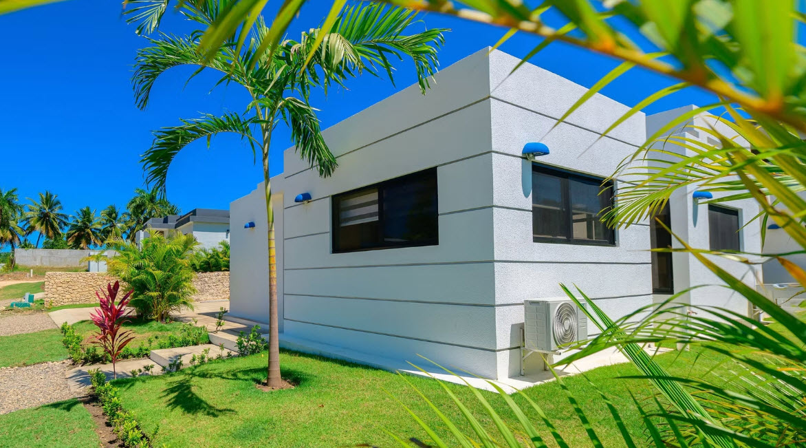 Modern white villa with palm trees and green lawn under blue sky.