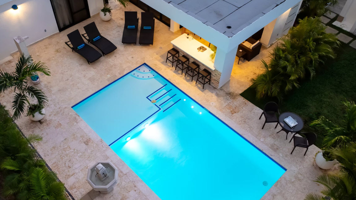 Luxury villa with illuminated pool, outdoor bar, and lounge chairs