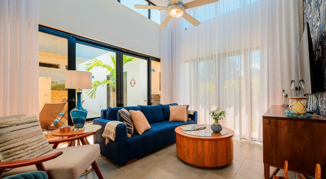 Modern living room with a deep blue sofa, large windows, and a ceiling fan