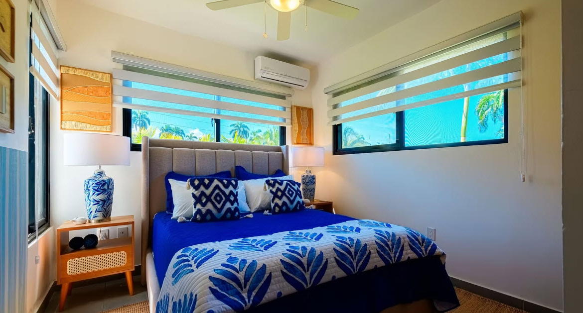 Modern bedroom with blue and white tropical bedding, large windows, and palm tree views.