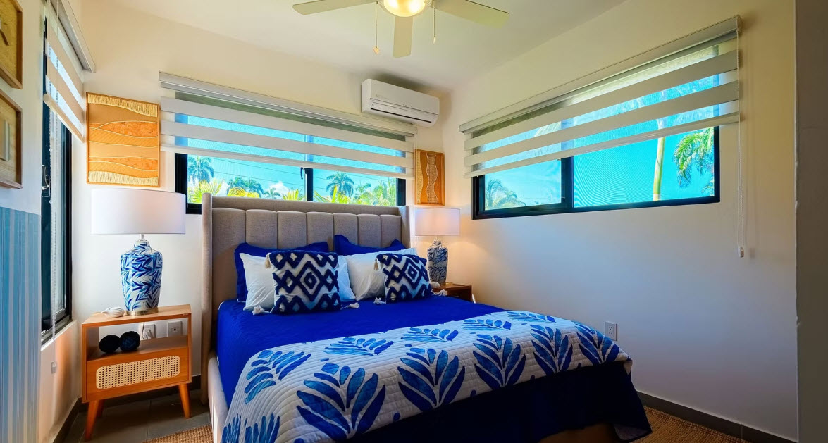 Modern bedroom with blue and white tropical bedding, large windows, and palm tree views.