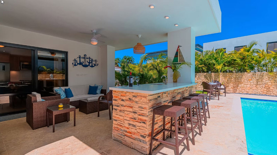 Outdoor bar with stools, seating area, and pool in a tropical setting.