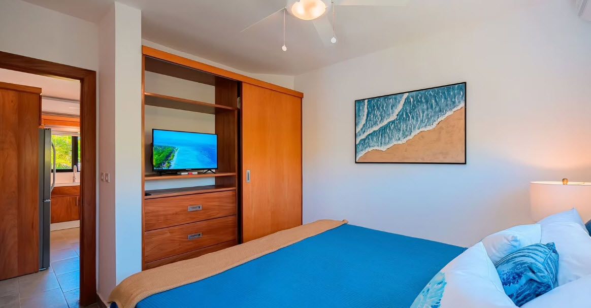 Modern bedroom with blue bedding, wooden closet, and ocean wave art