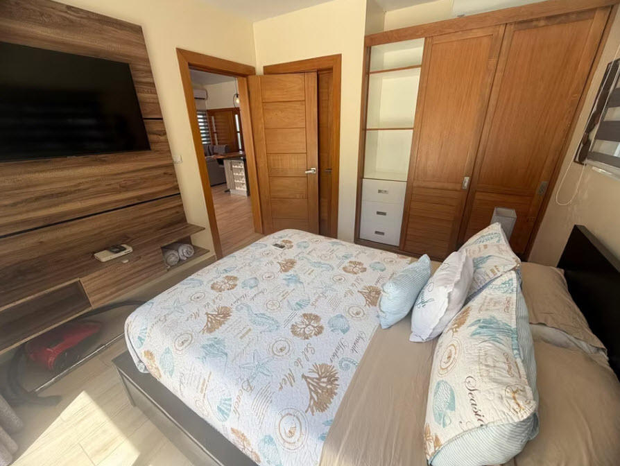 Modern bedroom with a queen-size bed, wooden wardrobe, and TV.