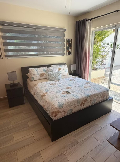 King-size bed with coastal-themed bedding in a bright bedroom with sliding glass doors.