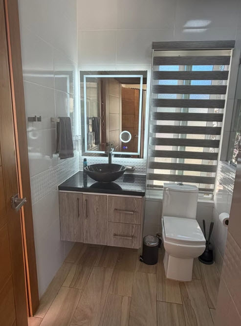 Modern bathroom with a floating vanity, vessel sink, backlit mirror, and toilet.
