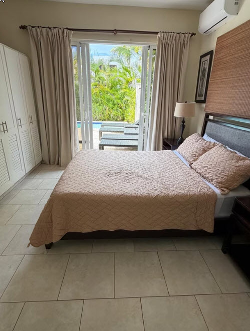 Bedroom with a queen bed, air conditioning, and a view of a tropical pool area.