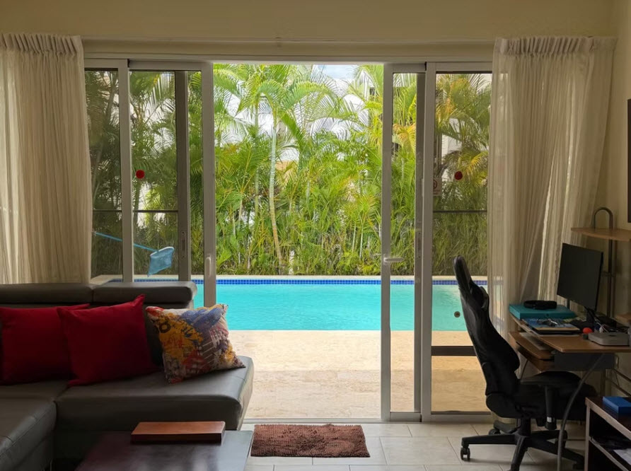View of a tropical pool and palm trees from a living room with a desk