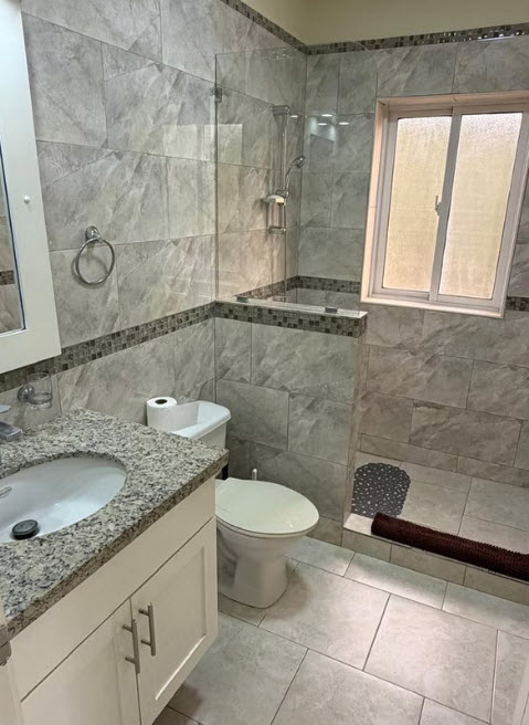 Modern bathroom with gray tile, glass shower, vanity, and toilet
