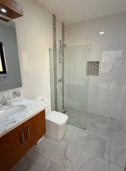 Modern bathroom with white tiled walls, marble floors, wooden vanity, and glass-enclosed shower.