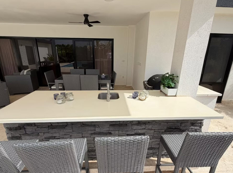 Modern outdoor kitchen with a stone-clad island, bar stools, and a grill.