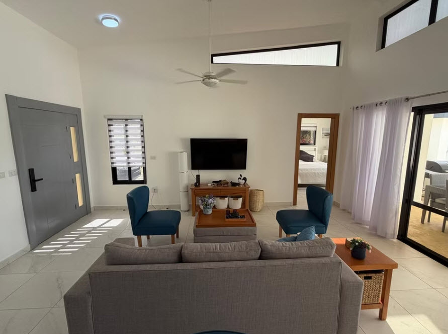 Modern living room with grey sofa, blue chairs, TV, and large windows