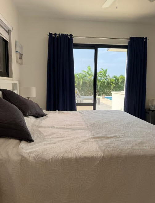 Bedroom with a view of a tropical pool and palm trees