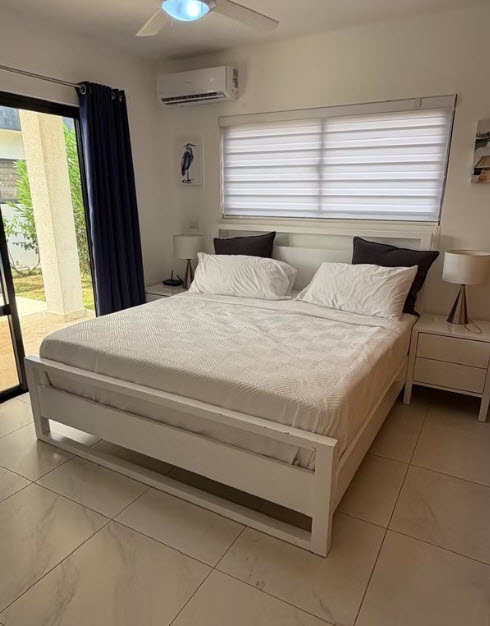 Modern white bedroom with a large bed, air conditioning, and a view of a tropical garden.