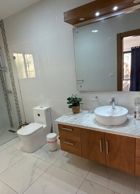 Modern white bathroom with wooden vanity, vessel sink, and walk-in shower.