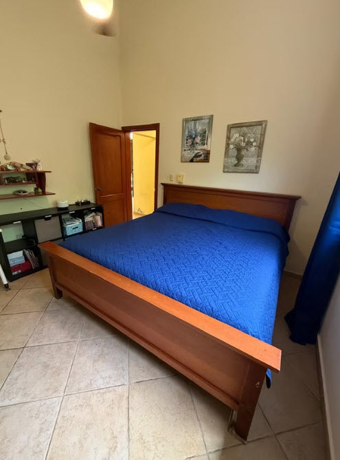 Bedroom with large wooden bed, blue quilted comforter, and tiled floor