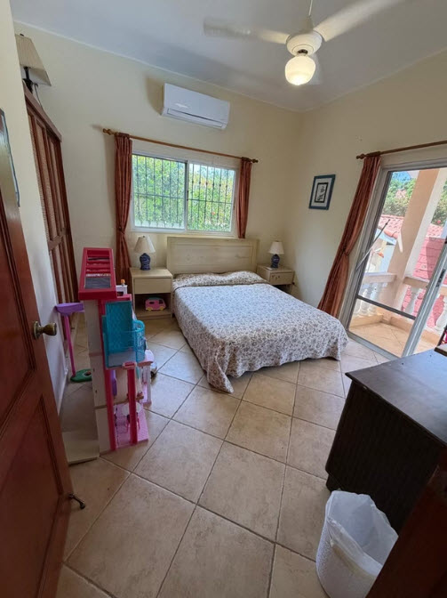 Cozy bedroom with a queen bed, dresser, and children's dollhouse.