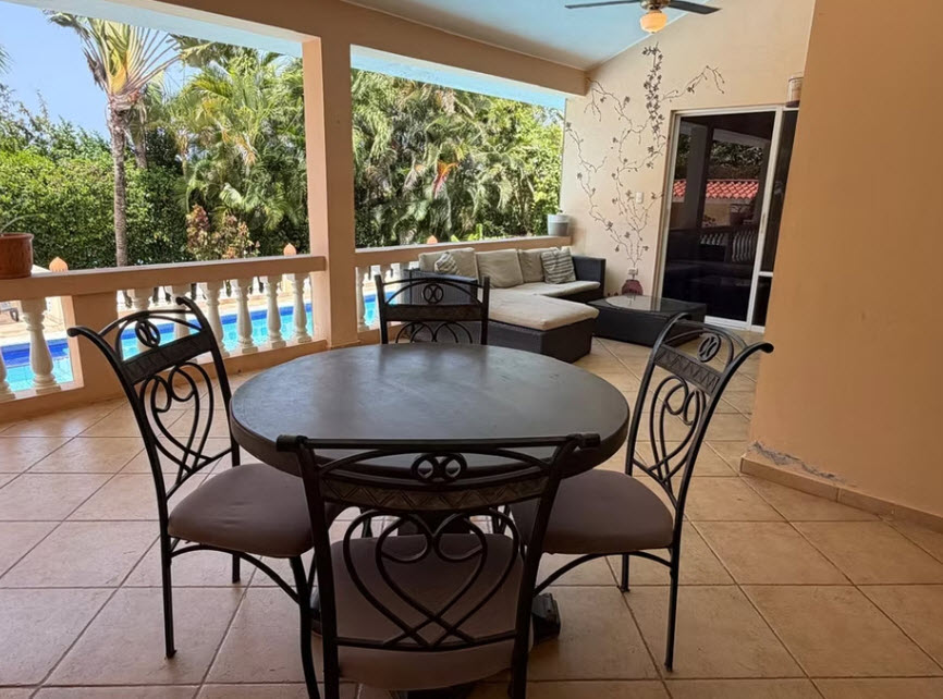Outdoor patio dining set with pool and lush greenery in background