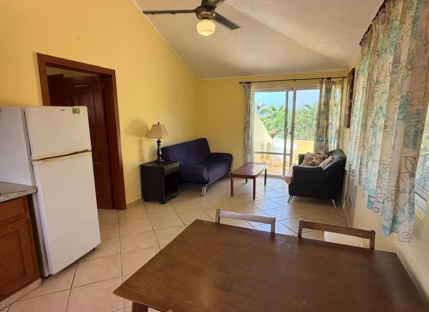 Bright living room with yellow walls, sofa, armchair, and sliding door to balcony.