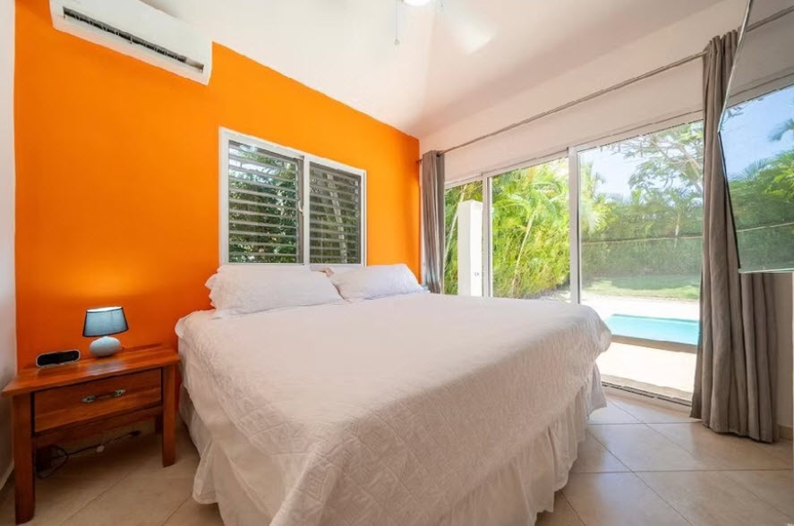 Bright tropical bedroom with orange accent wall and pool view