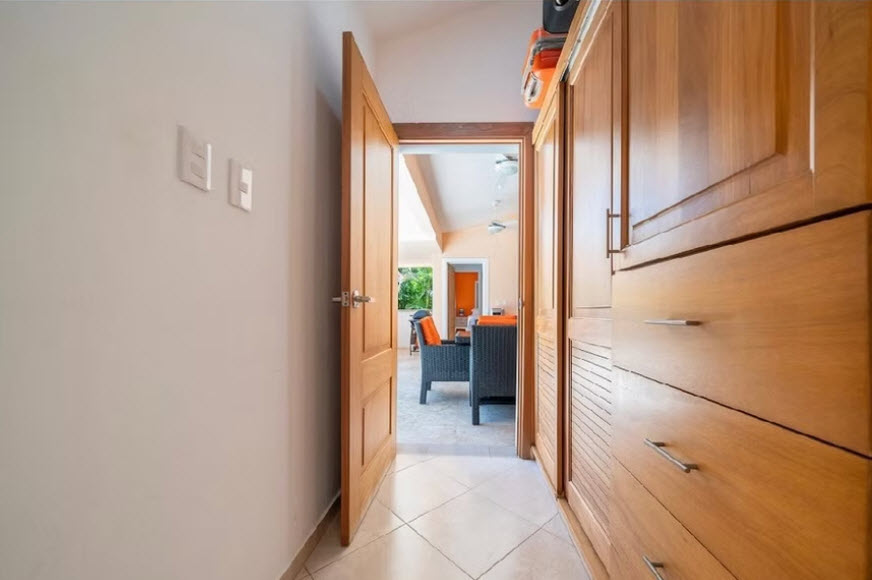 Hallway with open wooden door leading to a living area with orange accents.