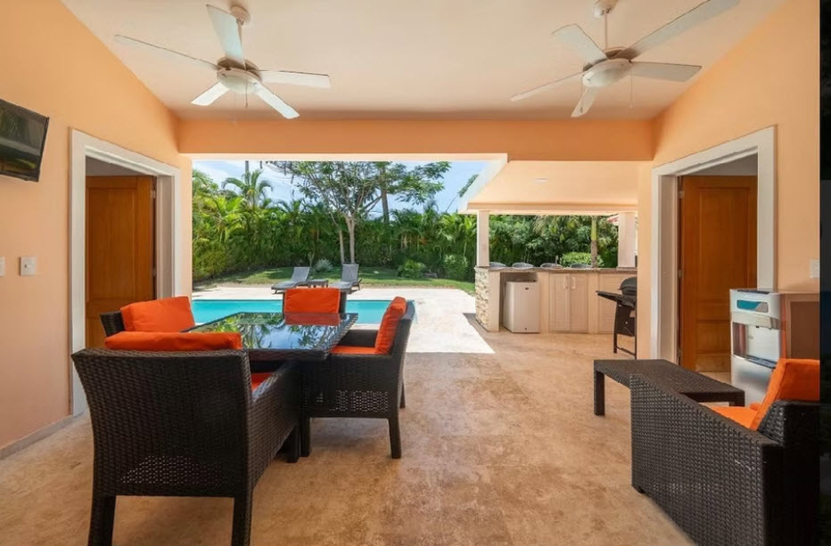 Outdoor patio with dining table, pool, and grill area in tropical setting