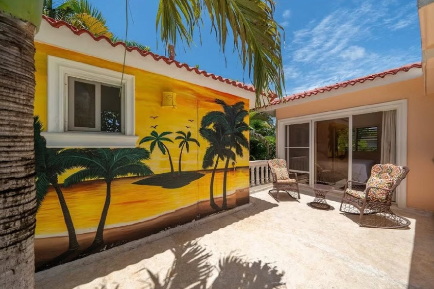 Vibrant mural of palm trees and sunset on a yellow building with outdoor seating.