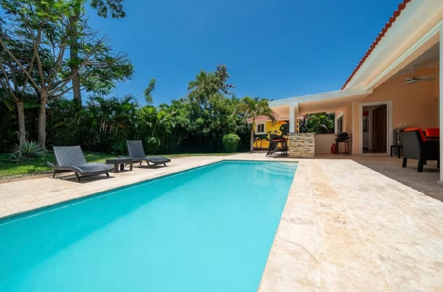 Luxury villa with turquoise pool, lounge chairs, and tropical garden